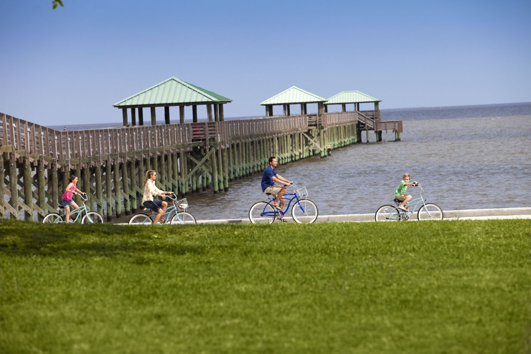 People biking along the coast, with a pier stretching out over the water